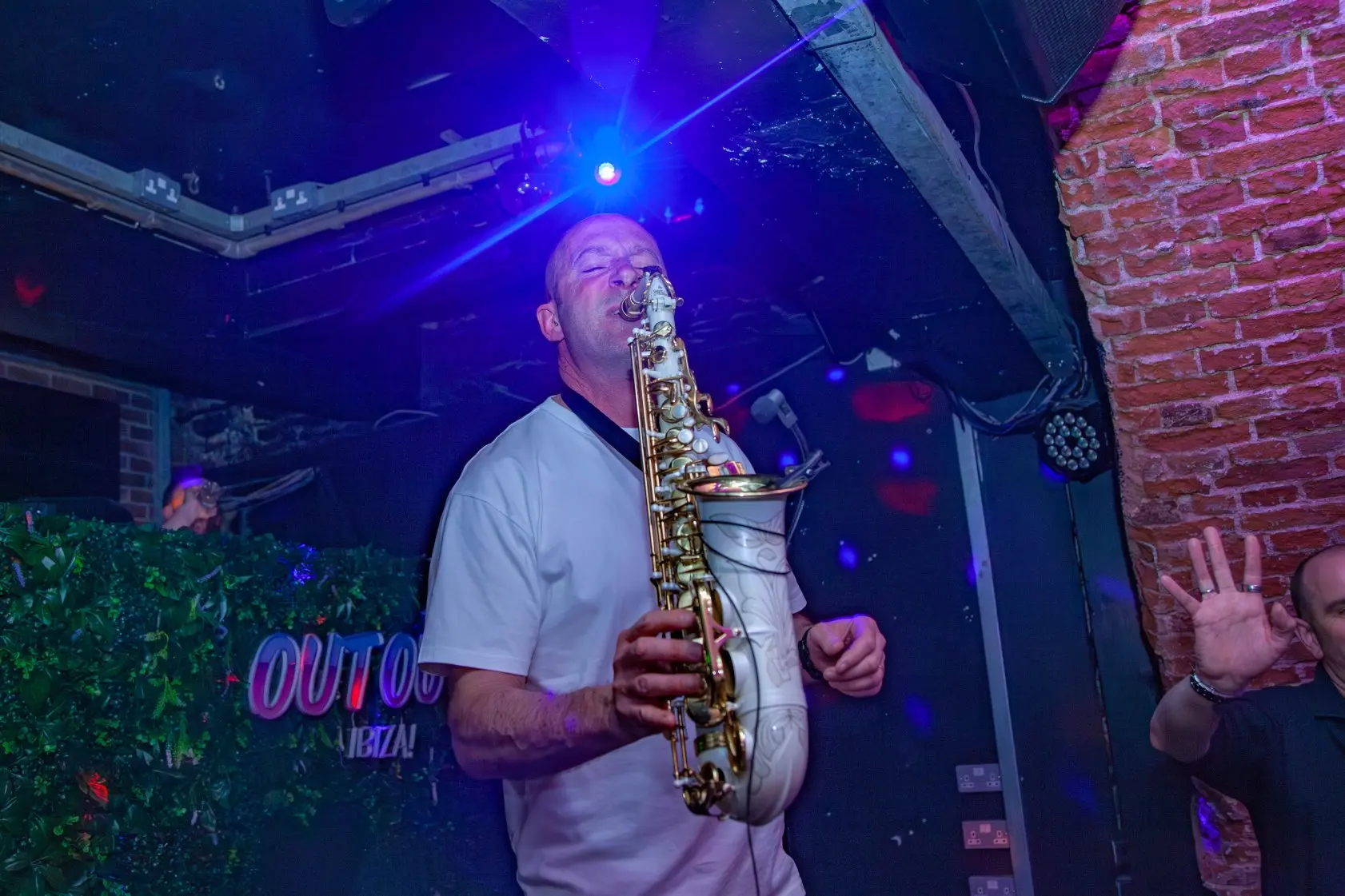 A saxophone player performing live music in the nightclub behind a bright blue light